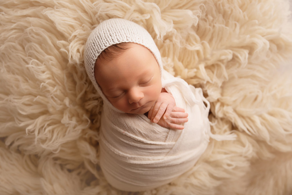 newborn baby boy with bonnet on cream fur