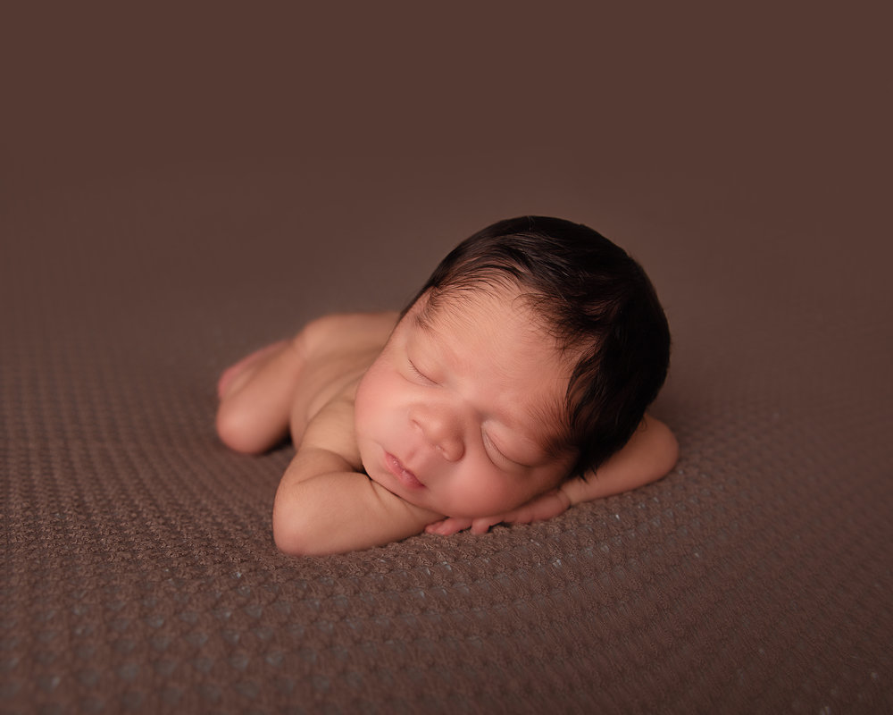 sleeping newborn baby boy on brown backdrop