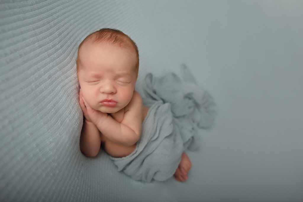 side lying pose newborn baby boy on mint backdrop