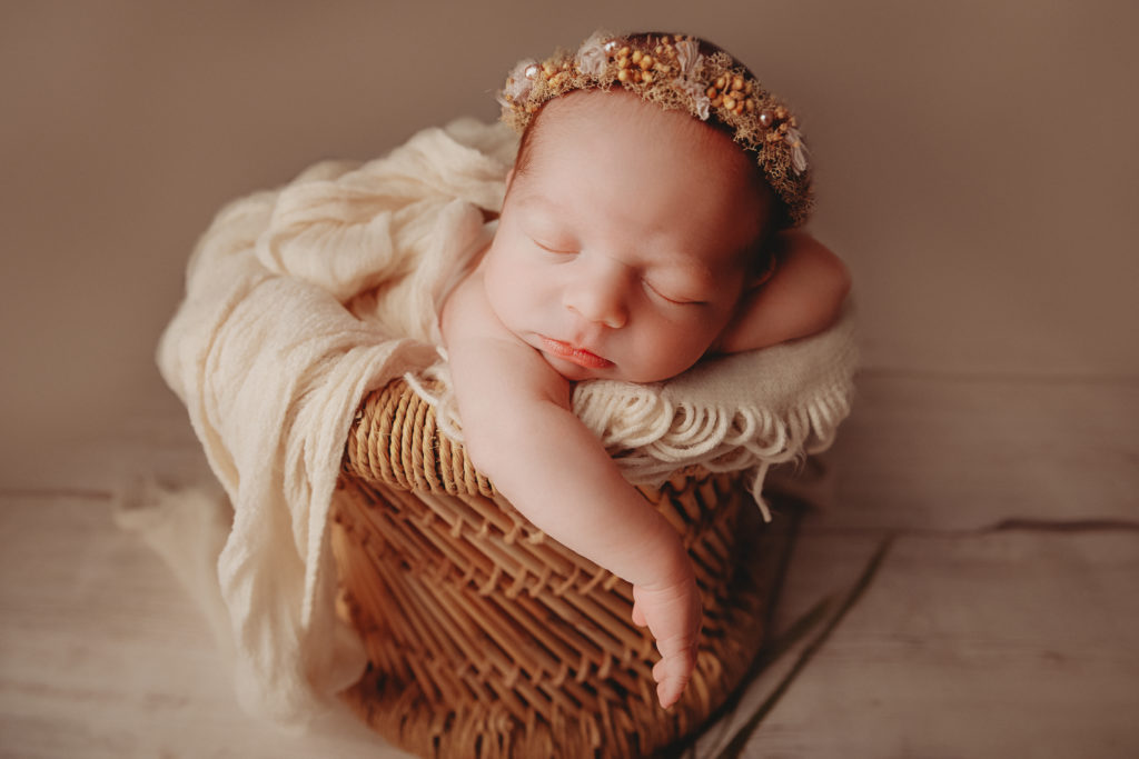 newborn baby in bamboo basket with arm hanging down