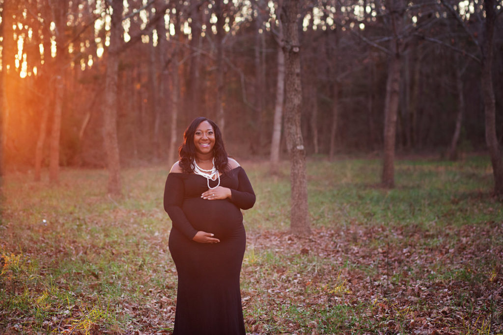 pregnant woman holding belly in forest at sunset