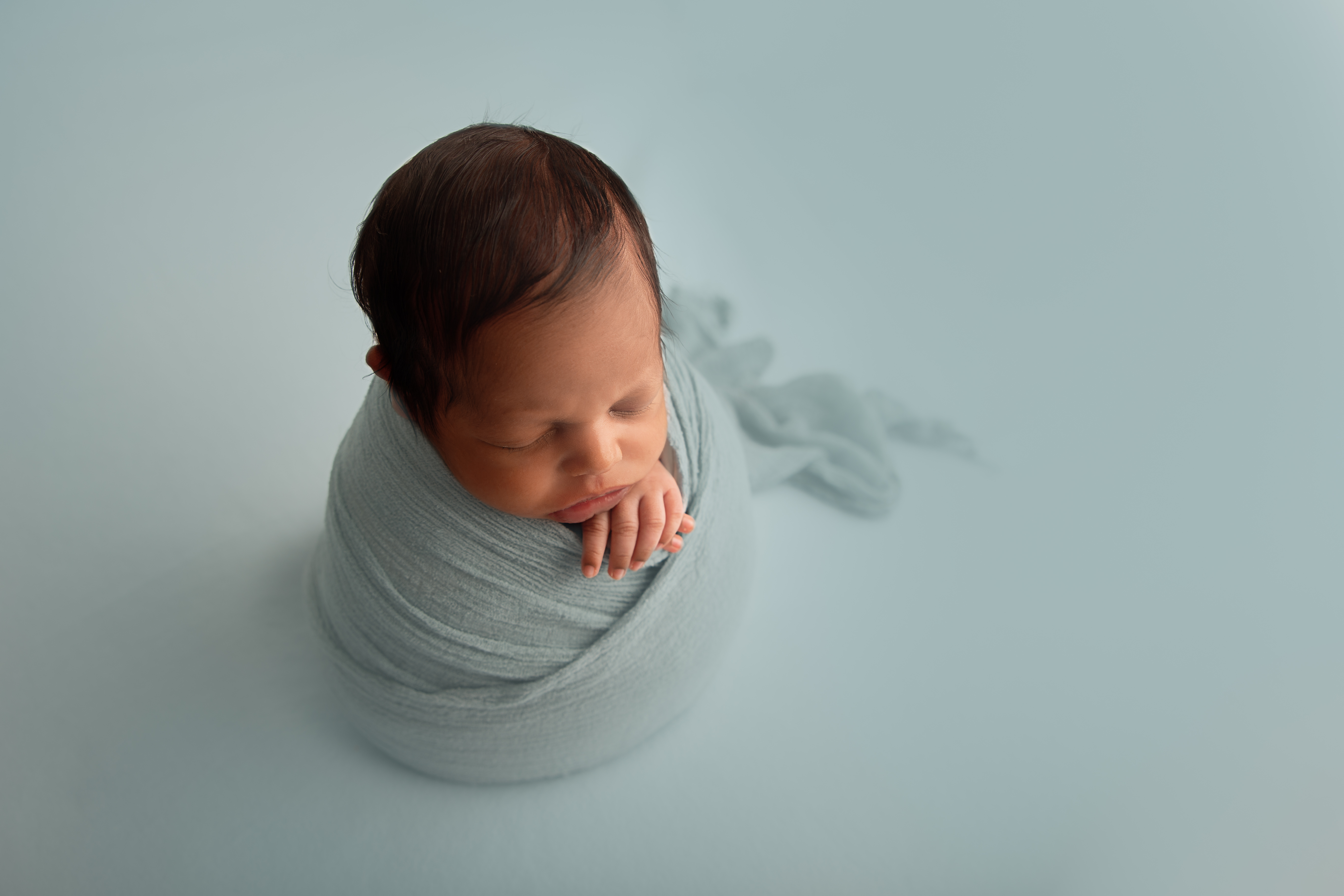 newborn boy on light blue backdrop upright swaddled